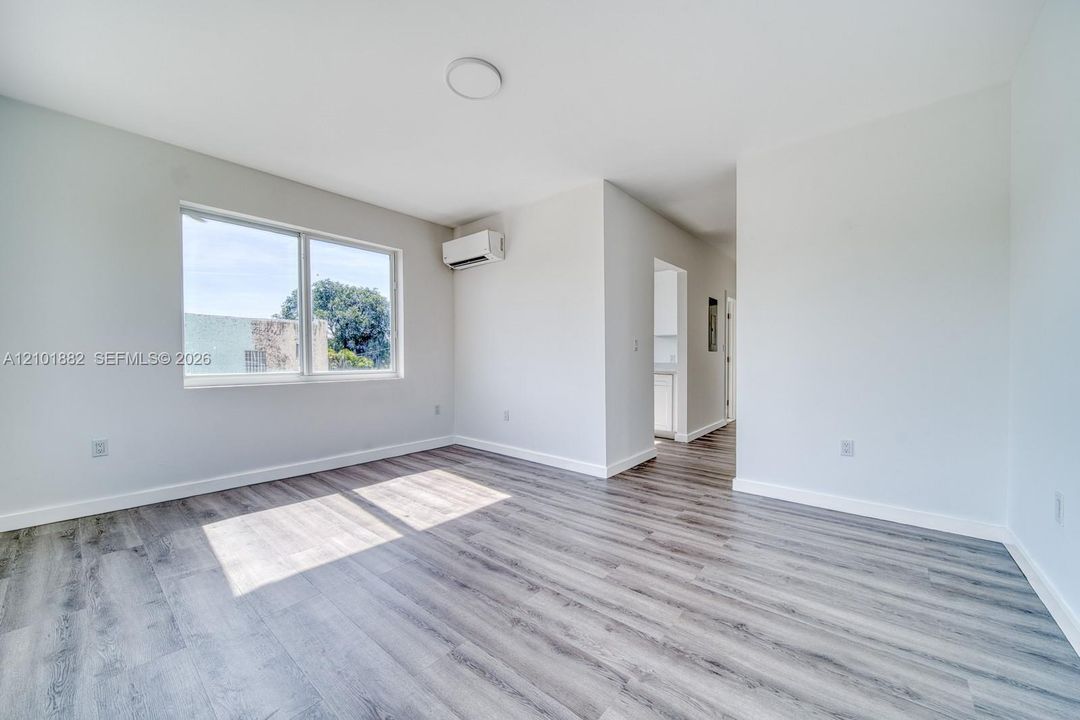 Bright interior space featuring wood-finish flooring, a wall-mounted climate control unit, and a large window