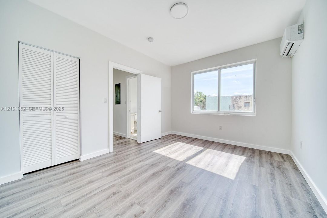 Room featuring wood-finish flooring, a wall-mounted ductless air conditioning unit, sliding window with exterior view, and a closet with bifold louvered doors