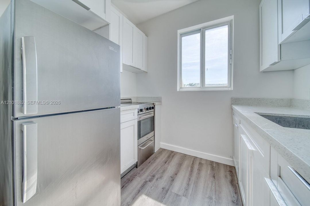 Kitchen featuring white shaker-style cabinetry, stainless steel appliances, speckled stone-finish countertops, and wood-finish flooring