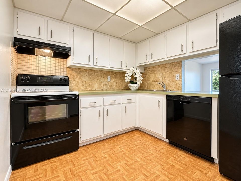 Kitchen featuring white cabinetry with metallic pulls, solid surface countertops, black appliances, square tile backsplash, and parquet flooring