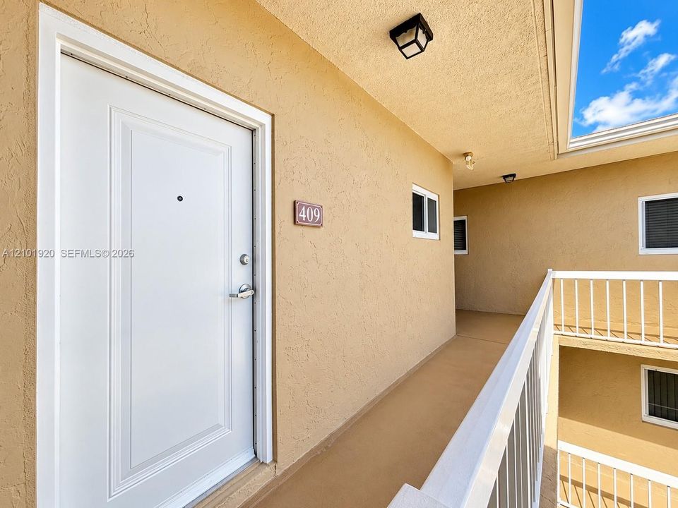 Entryway featuring a white paneled door with a metallic deadbolt, exterior wall-mounted lighting, and a white metal safety railing