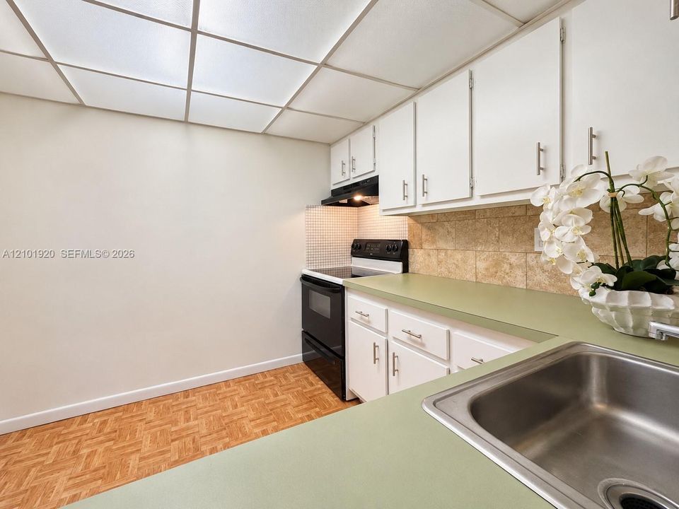 Kitchen featuring white cabinetry with brushed metal hardware, solid-surface countertops, tile backsplash, and parquet flooring