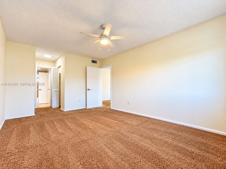 Neutral wall paint, plush carpeting, ceiling fan with integrated lighting, and interior swing doors
