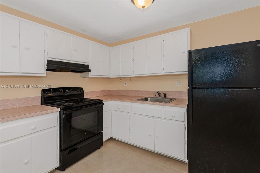 Kitchen featuring white shaker-style cabinetry, solid-surface countertops with integrated backsplash, a black range with hood, and a drop-in stainless steel sink