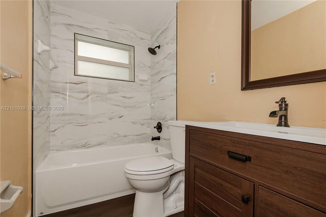 Bathroom featuring a wood-finish vanity with a rectangular sink, patterned tile shower surround, matte black fixtures, and a recessed window