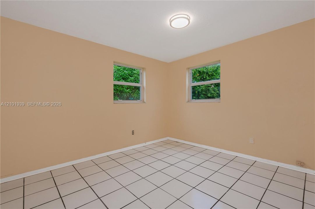 Neutral-toned interior space featuring light-colored ceramic tile flooring, two windows with exterior greenery, and a central flush-mount ceiling light fixture