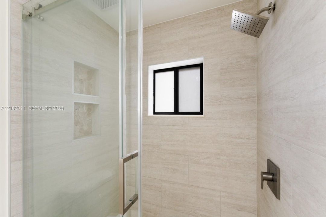 Glass-enclosed shower featuring light-toned tile, dual recessed niches, a black-framed window, and a rain shower head