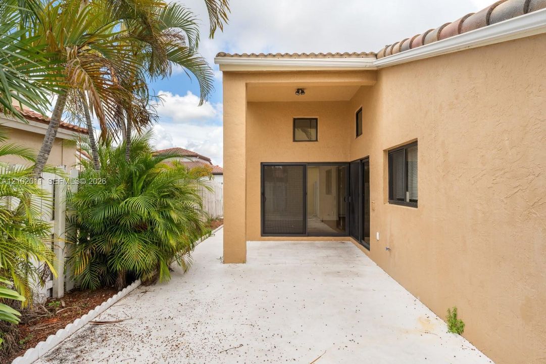 Private patio area with stucco exterior, sliding glass doors, multiple windows, and tropical landscaping