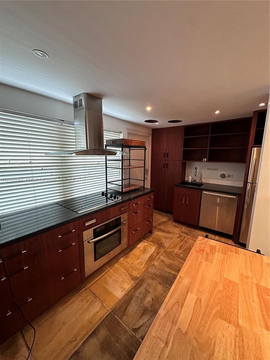 Kitchen featuring rich wood cabinetry, stainless steel appliances, dark countertops, and varied stone tile flooring