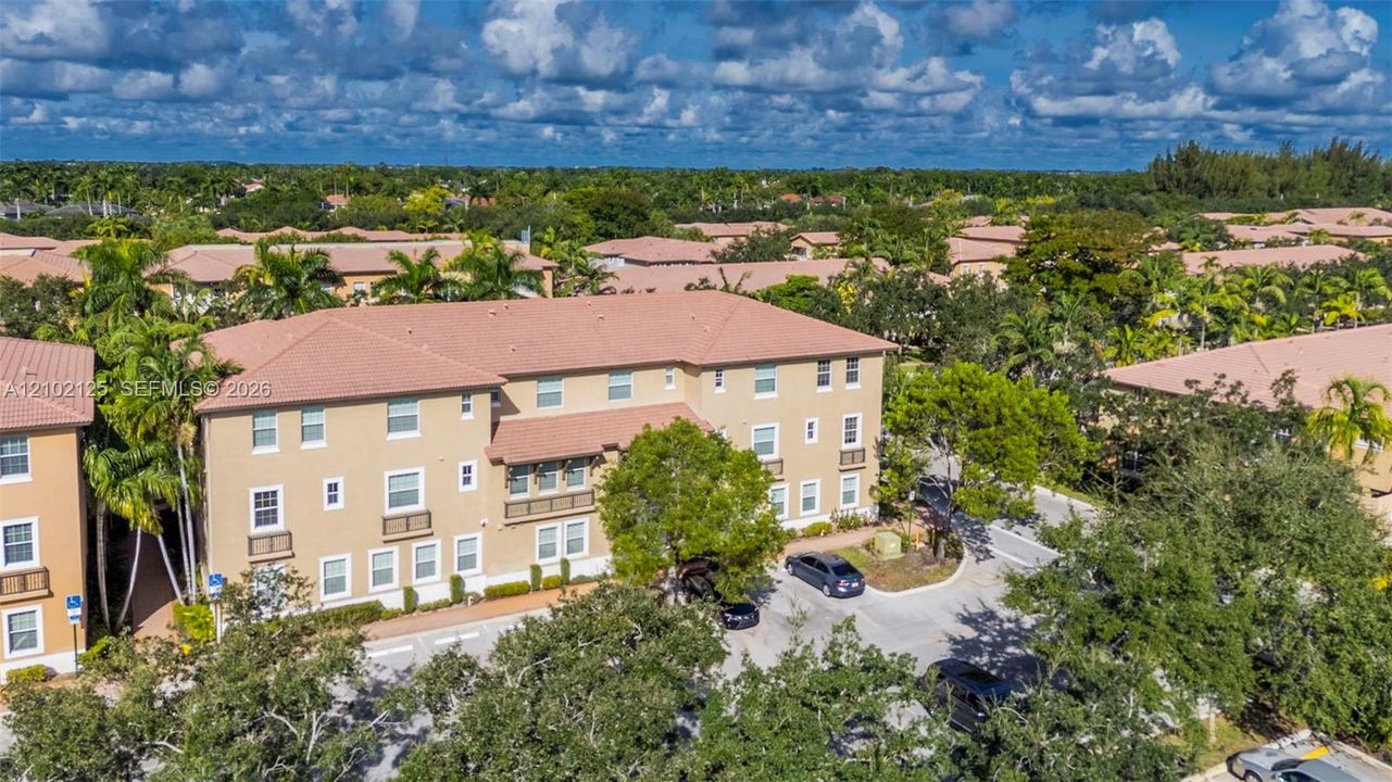 Multi-story residential building featuring a tile roof, stucco exterior, decorative iron-rail balconies, and dedicated surface parking