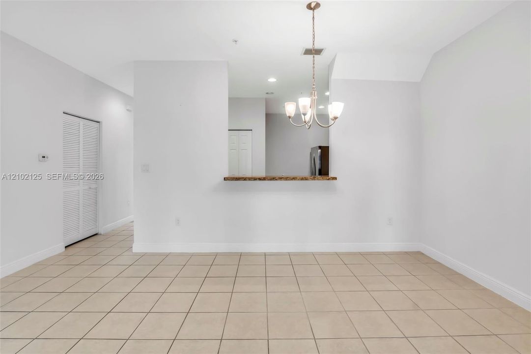 Dining area featuring ceramic tile flooring, a pass-through breakfast bar with a stone-finish countertop, a multi-arm chandelier, and louvered closet doors
