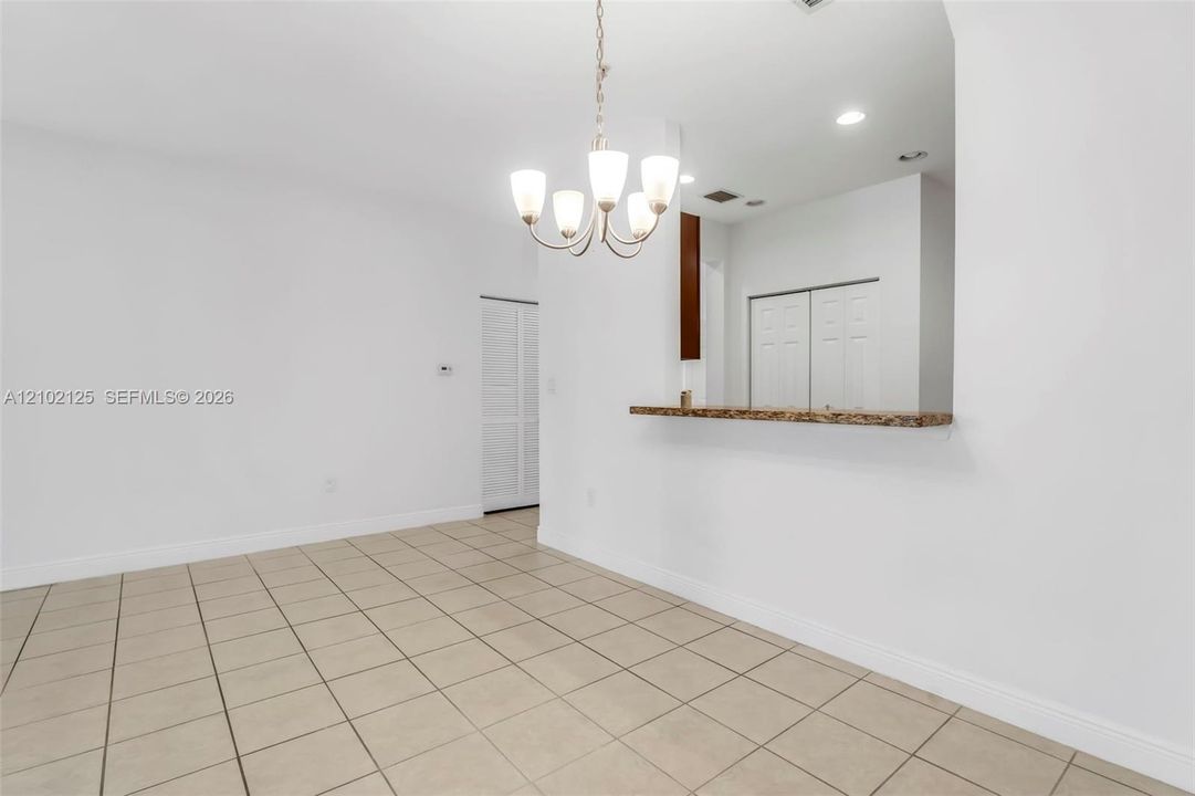 Ceramic tile flooring, multi-arm metal chandelier, pass-through opening with stone-finish countertop, and louvered closet doors