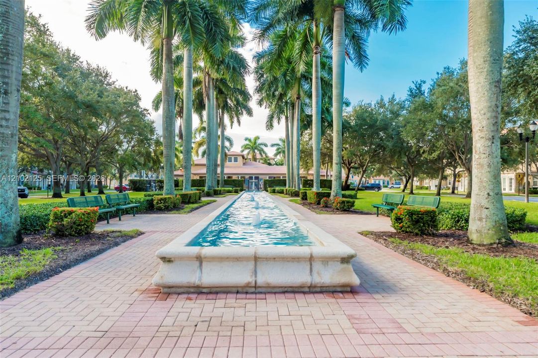 Central water feature with stone coping, lined by mature palm trees and brick-paver pathways