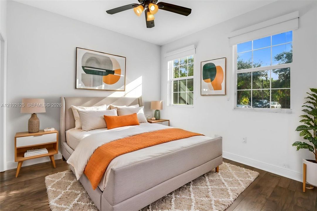 Virtually Stage - Bedroom featuring wood-finish flooring, dual windows with grid detailing, and a multi-blade ceiling fan with integrated lighting