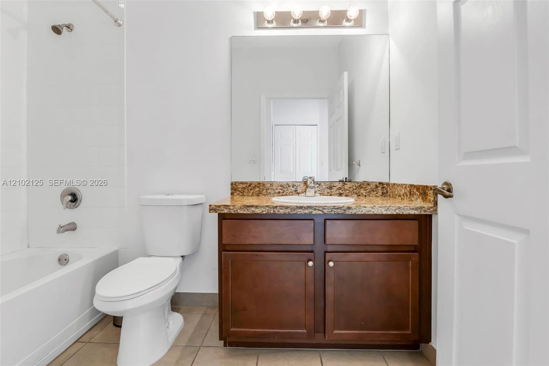 Bathroom featuring a stained wood vanity with a stone countertop, an integrated oval sink, a wall-mounted light fixture, and a tile-surround shower and tub combination