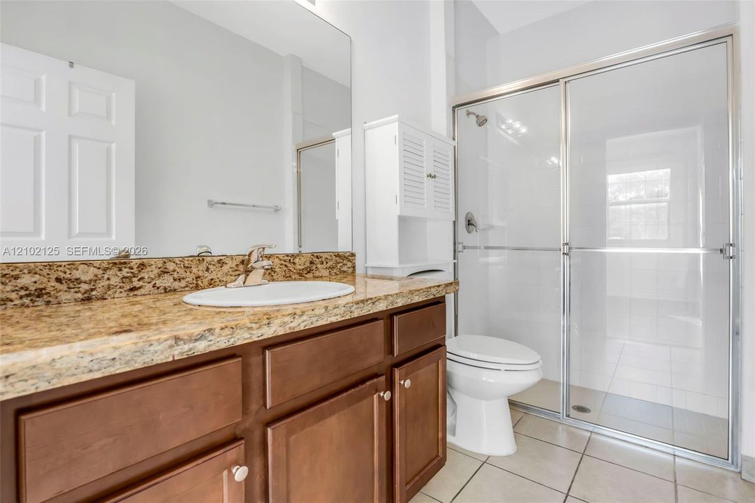 Bathroom featuring wood cabinetry, stone-finish vanity countertop with an integrated basin, large wall-mounted mirror, and a walk-in shower enclosure with a glass door