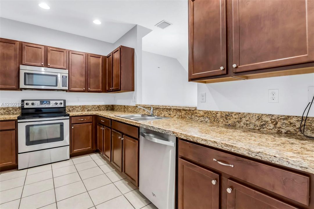 Kitchen featuring medium-tone wood cabinetry, stone-patterned countertops, stainless steel appliances, and tile flooring