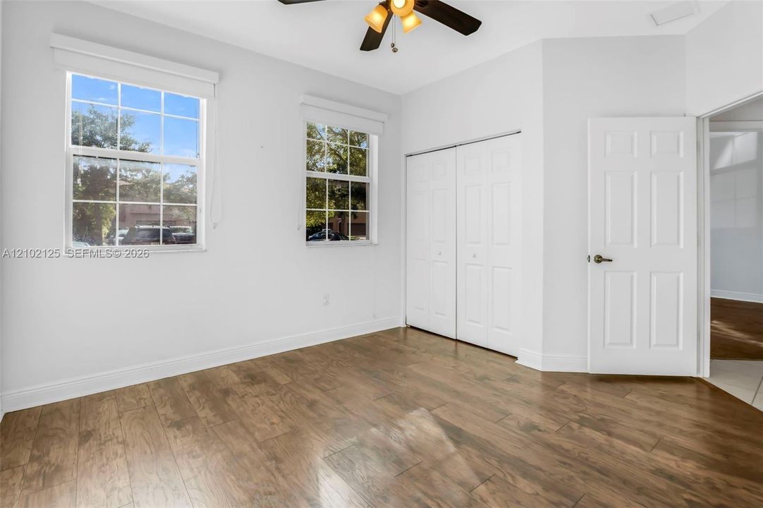 Room featuring wood-finish flooring, dual windows, a ceiling fan with integrated lighting, and a double-door closet