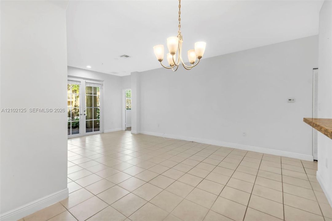 Neutral-toned tile flooring, multi-pane glass door, and overhead multi-light chandelier