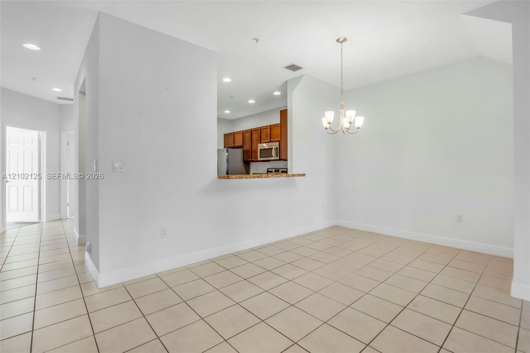Dining area featuring ceramic tile flooring, a multi-light chandelier, and a breakfast bar pass-through with wood-finish cabinetry