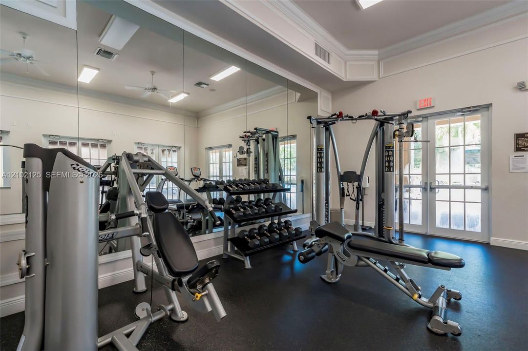 Fitness room featuring floor-to-ceiling mirrors, rubberized flooring, crown molding, and double-door entry with glass panes