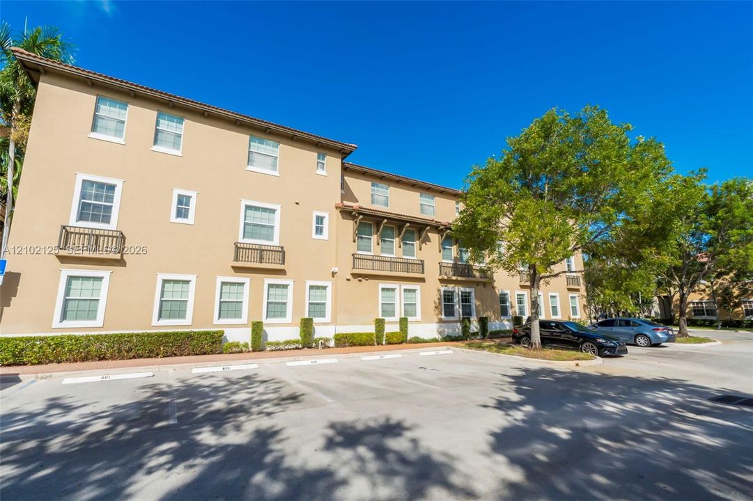 Stucco exterior featuring multi-story architectural detailing, decorative iron railings, and dedicated paved parking