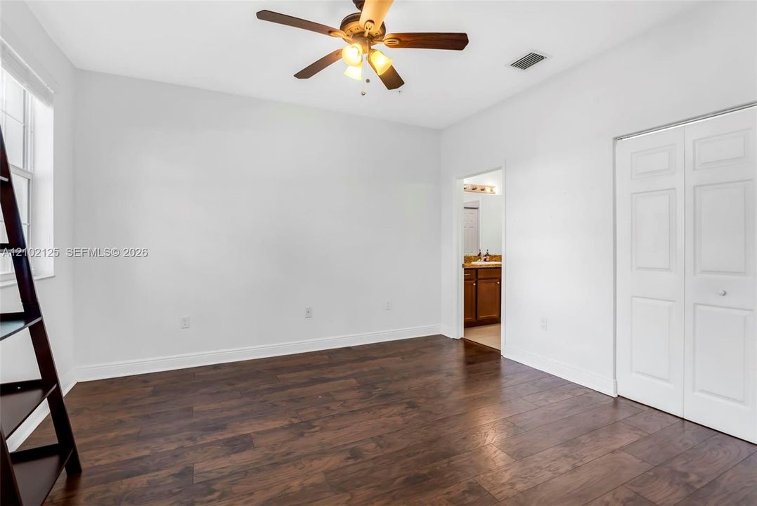 Room featuring dark wood-finish flooring, white walls, a ceiling fan with integrated lighting, and white bifold closet doors