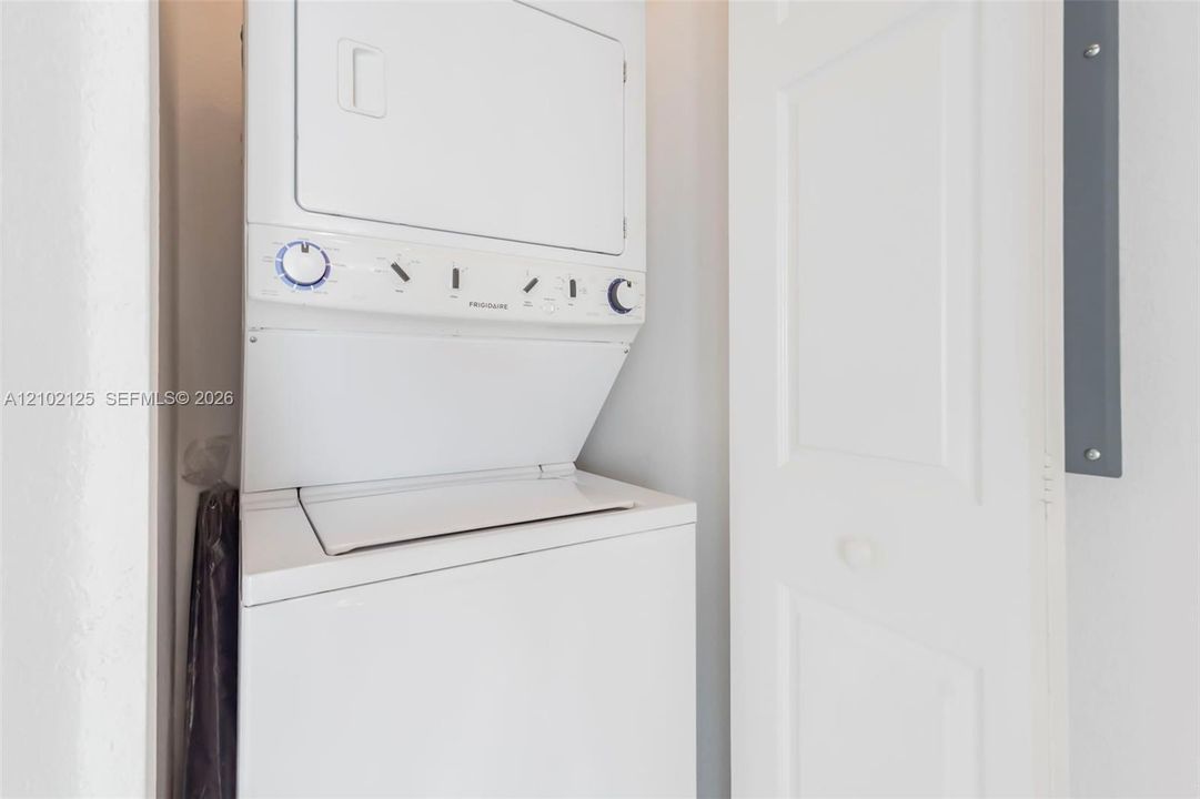 Stacked white laundry unit housed within a dedicated closet featuring a solid-core panel door