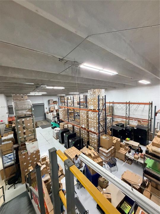 Large warehouse space featuring exposed concrete ceiling beams and fluorescent lighting