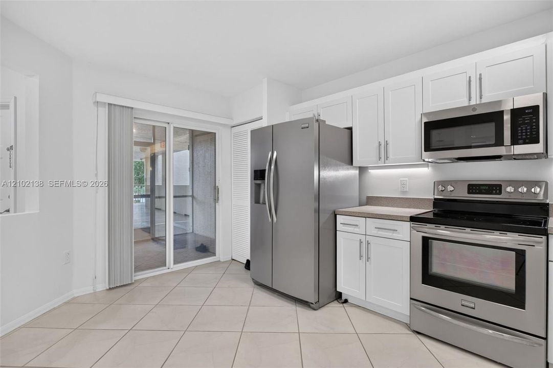 Kitchen featuring white shaker-style cabinetry, stainless steel appliances, neutral stone-finish countertops, tile flooring, and a sliding glass door