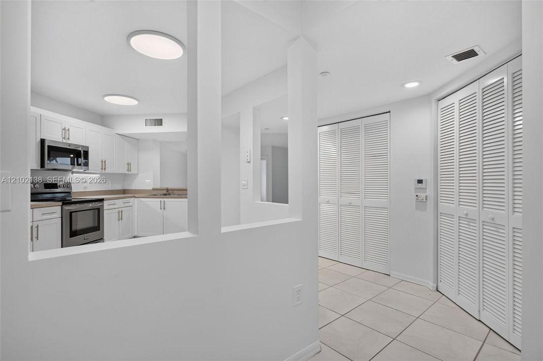 Kitchen featuring white cabinetry, stainless steel appliances, neutral stone-finish countertops, ceramic tile flooring, and dual bi-fold louvered closet doors