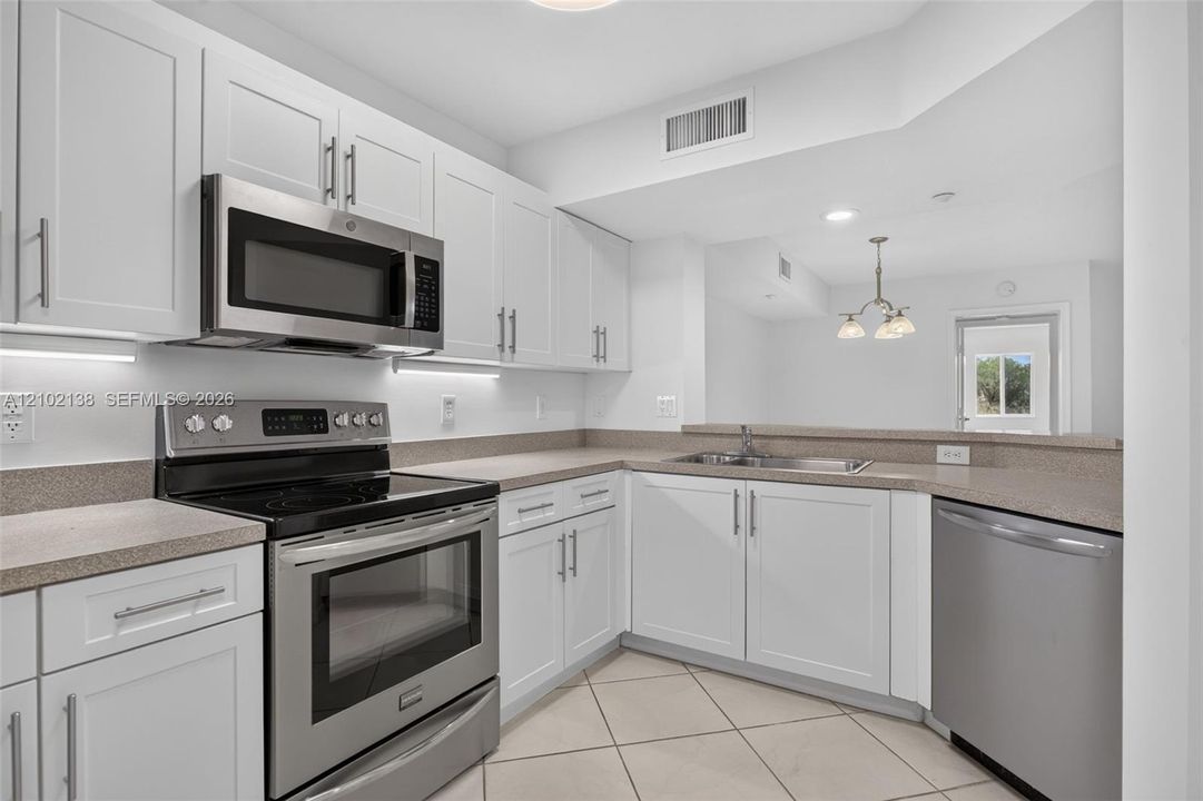 Kitchen featuring white shaker-style cabinetry, stone-finish countertops, stainless steel appliances, under-cabinet lighting, and tile flooring