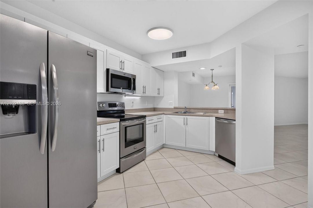 Kitchen featuring white shaker-style cabinetry, stainless steel appliances, neutral stone-finish countertops, and large-format tile flooring