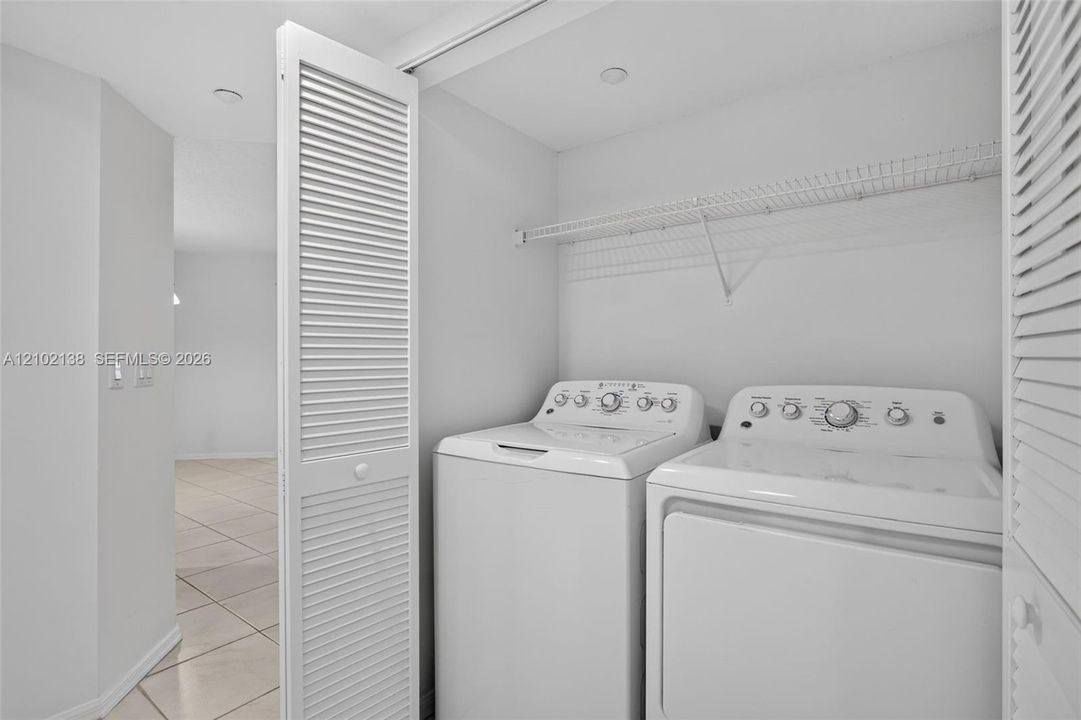 Laundry area featuring white louvered folding doors, built-in wire shelving, and tile flooring