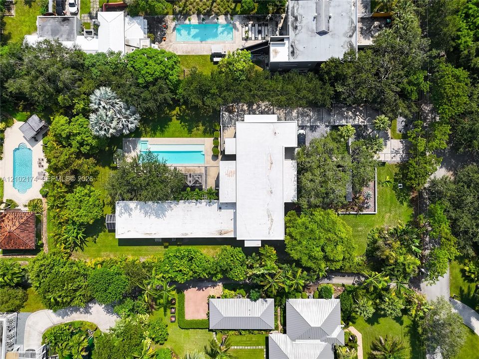 Aerial view of the property featuring a rectangular swimming pool, expansive green space, mature landscaping, and a multi-section roofline