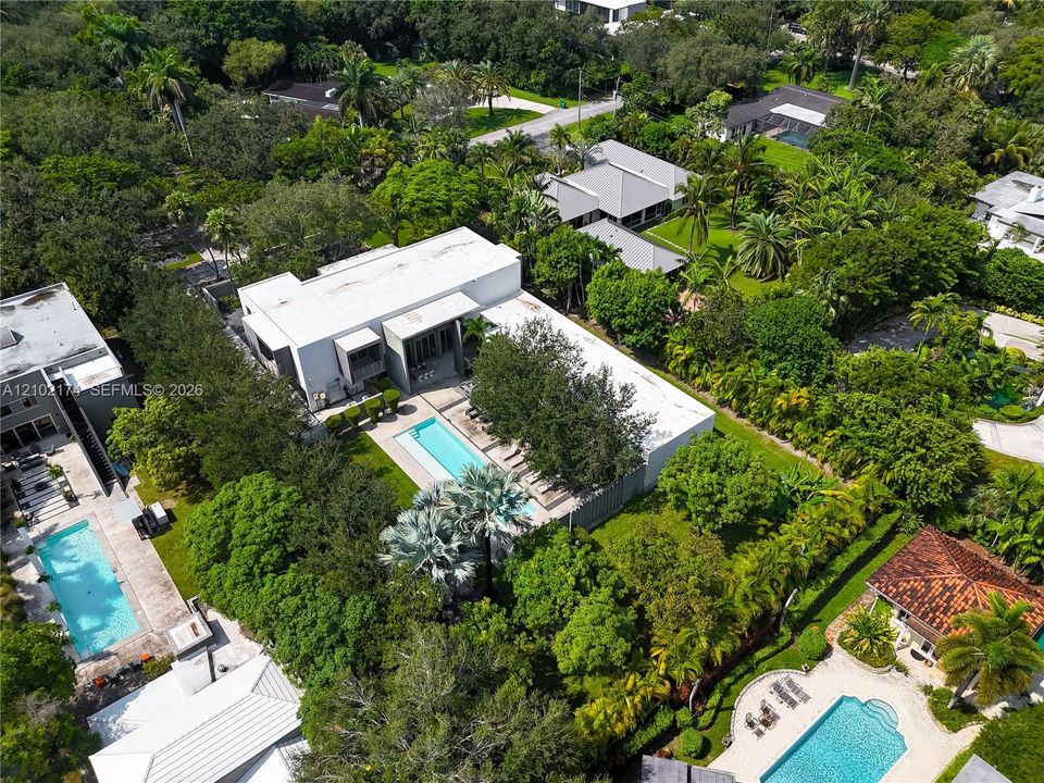 Aerial perspective of a multi-level contemporary estate featuring a rectangular swimming pool, integrated hardscaping, established perimeter landscaping, and mature foliage