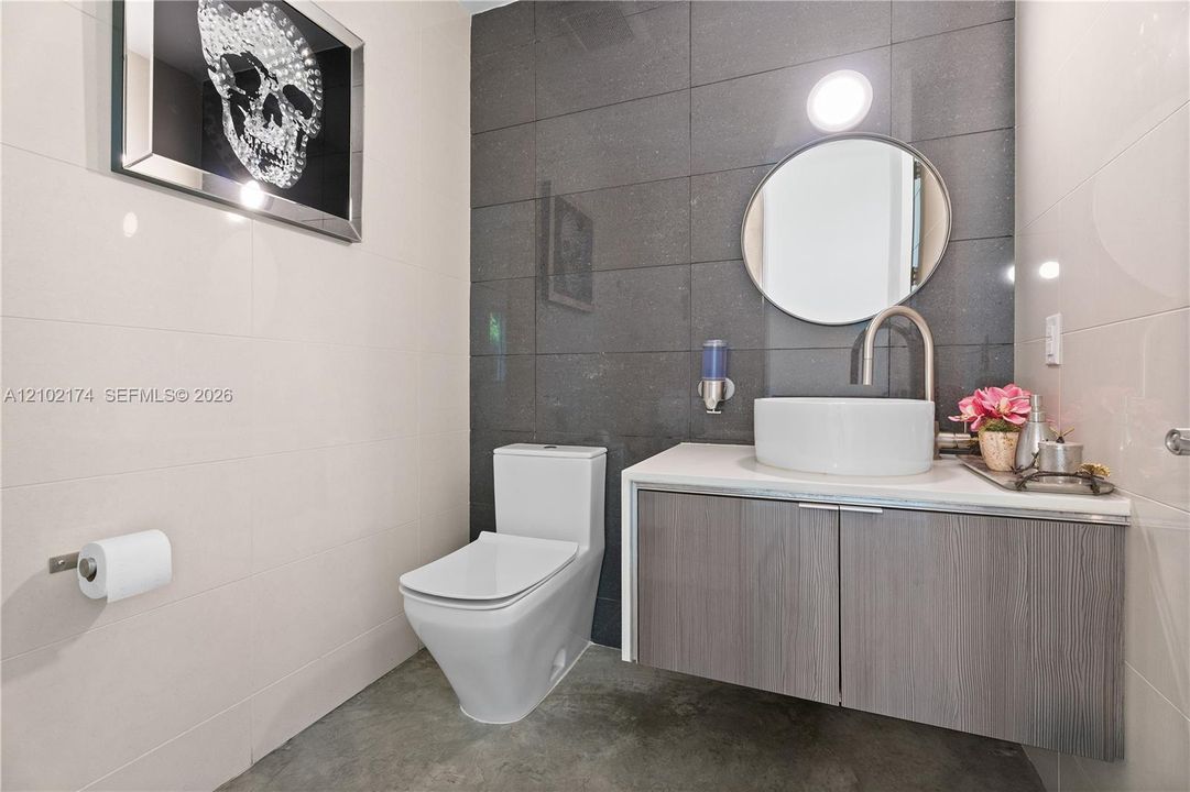 Floating vanity with a white vessel sink, polished countertop, circular mirror, and floor-to-ceiling dark tile accent wall