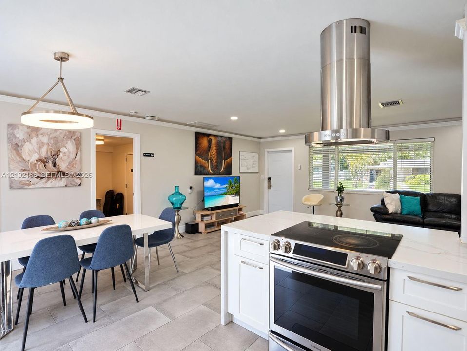 Kitchen featuring white cabinetry, quartz countertops, a stainless steel cylindrical range hood, and a built-in electric cooktop, complemented by neutral tile flooring throughout the area