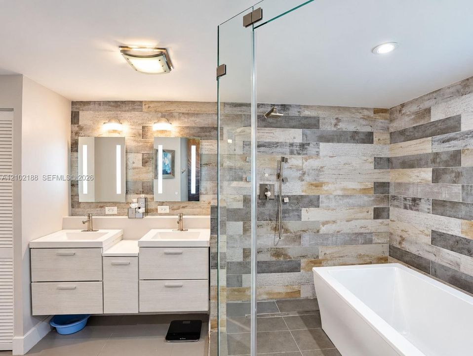 Dual-sink vanity with rectangular basins, integrated LED-lit mirrors, a glass-enclosed walk-in shower, freestanding soaking tub, and multi-toned wood-finish wall tile