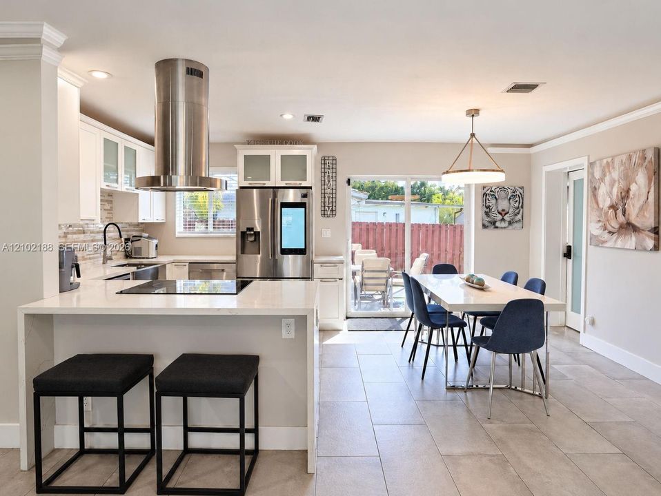 Kitchen featuring white cabinetry with glass-front uppers, stainless steel appliances including a cylinder range hood, quartz countertops, and large-format tile flooring