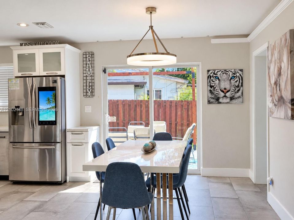 Modern kitchen featuring stainless steel refrigerator, white cabinetry with glass-panel upper doors, large-format tile flooring, and circular LED pendant lighting