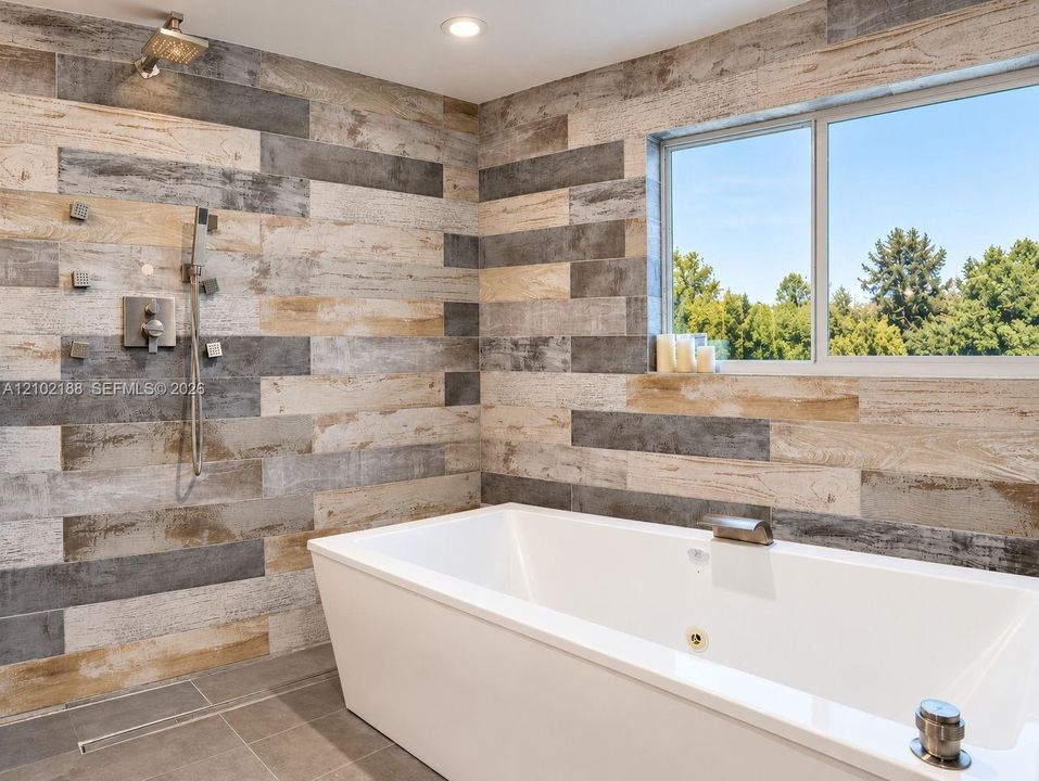 Freestanding soaking tub with a deck-mounted faucet, multi-head shower system, recessed lighting, and multi-toned wood-finish wall tile