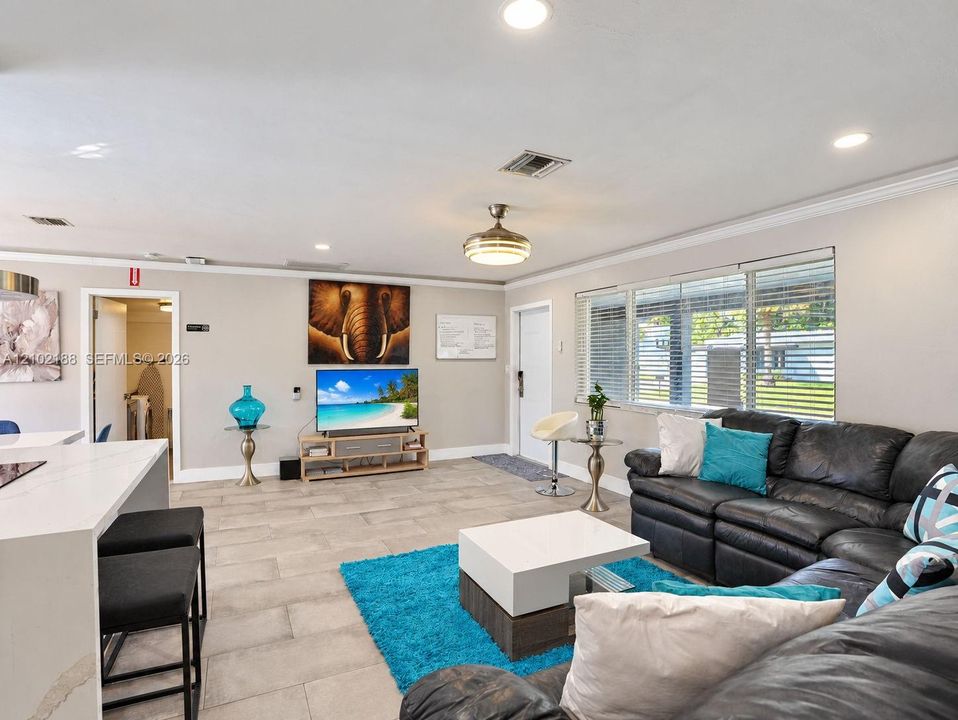 Open-concept interior featuring light-toned tile flooring, recessed ceiling lighting, a contemporary ceiling fan, and large windows with horizontal blinds