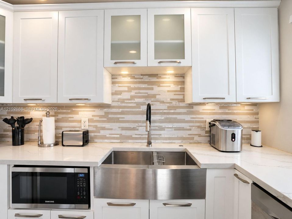Kitchen featuring white shaker-style cabinetry with glass-front uppers, solid surface countertops, a horizontal mosaic tile backsplash, and an undermount stainless steel farmhouse sink with a high-arc pull-down faucet