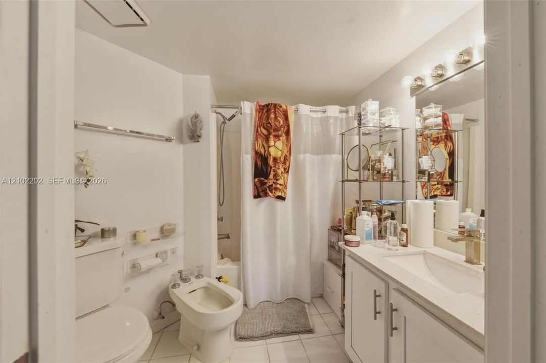 Bathroom featuring a white vanity with white cabinetry, a built-in shower, a toilet, a bidet, and wall-mounted lighting