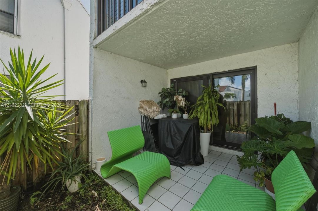 Covered outdoor patio with a tiled floor, sliding glass door access, exterior wall light, and a wooden privacy fence