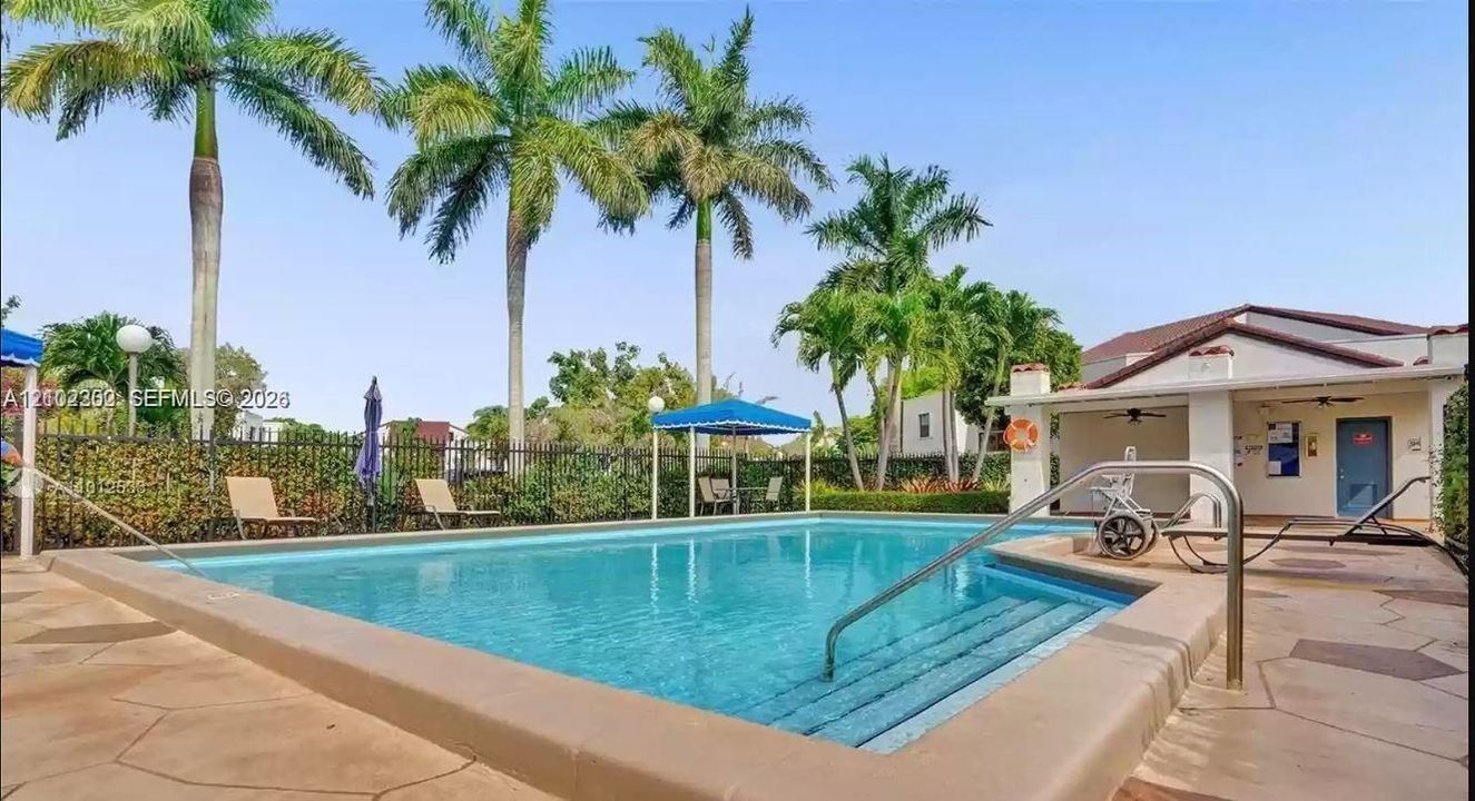Outdoor swimming pool with integrated steps, surrounded by a paved deck and mature palm trees