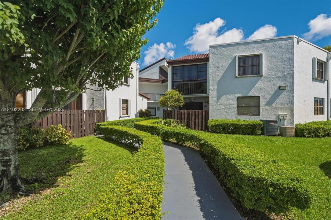 Manicured lawn with shaped hedges, mature tree, paved walkway, and privacy fencing