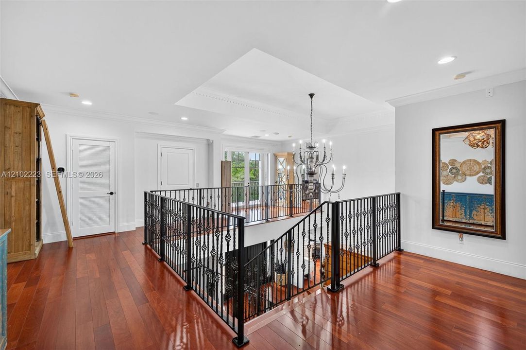 An impressive, second floor Landing overlooks the grand foyer below, showcasing, beautiful hardwood floors, decorative rod, iron railings, and striking chandelier. The architectural design creates a wonderful sense of grandeur while connecting the upper level living spaces.