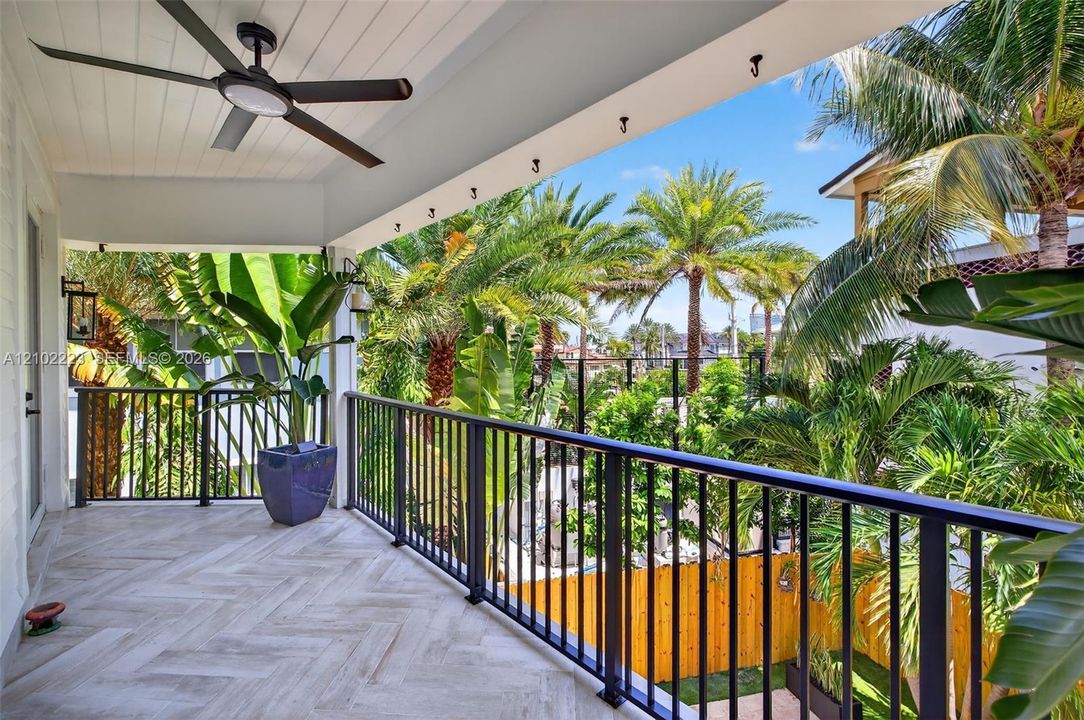 An expansive covered balcony of the primary suite offers a beautiful Tropical escape, surrounded by swaying palms and lush greenery with generous space for outdoor lounging, beautiful tile flooring and a cooling ceiling fan. It’s an inviting retreat for morning coffee evening cocktails are simply enjoying the south Florida breeze.